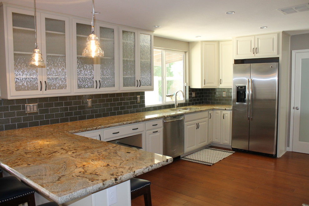 Mid-sized transitional u-shaped dark wood floor and brown floor eat-in kitchen photo in Phoenix with an undermount sink, raised-panel cabinets, white cabinets, granite countertops, green backsplash, glass tile backsplash, stainless steel appliances and a peninsula
