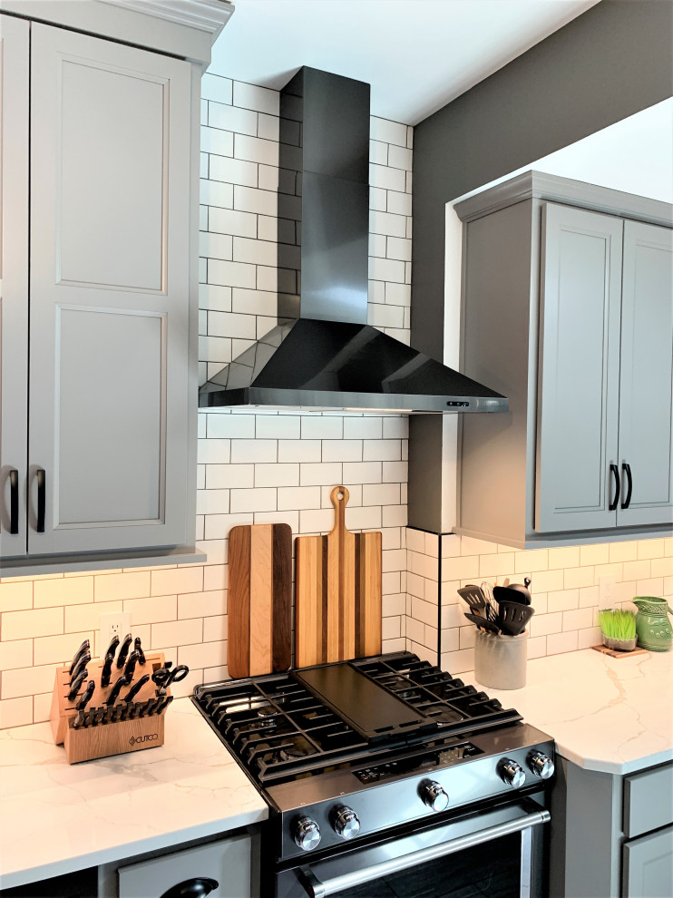 Inspiration for a mid-sized traditional l-shaped separate kitchen in Other with an undermount sink, flat-panel cabinets, grey cabinets, quartz benchtops, white splashback, subway tile splashback, black appliances, vinyl floors, with island, grey floor and white benchtop.