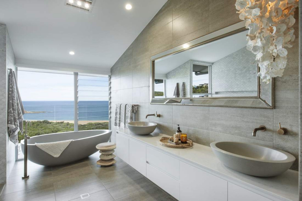 Inspiration for a large beach style master bathroom in Other with recessed-panel cabinets, white cabinets, a freestanding tub, gray tile, grey walls, a vessel sink, grey floor, white benchtops, a double vanity and a floating vanity.