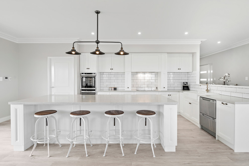 Design ideas for a mid-sized transitional galley eat-in kitchen in Perth with a farmhouse sink, recessed-panel cabinets, white cabinets, solid surface benchtops, white splashback, ceramic splashback, stainless steel appliances, vinyl floors and with island.