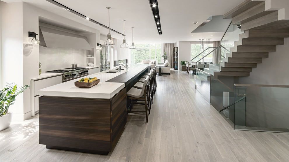 This is an example of a large contemporary l-shaped open plan kitchen in Sydney with an integrated sink, white cabinets, light hardwood floors, with island and brown floor.