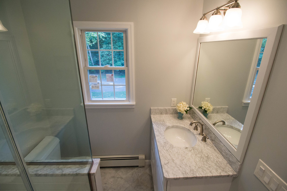 Example of a small transitional master white tile and ceramic tile marble floor and gray floor corner shower design in Newark with shaker cabinets, white cabinets, a two-piece toilet, gray walls, an undermount sink, marble countertops and a hinged shower door