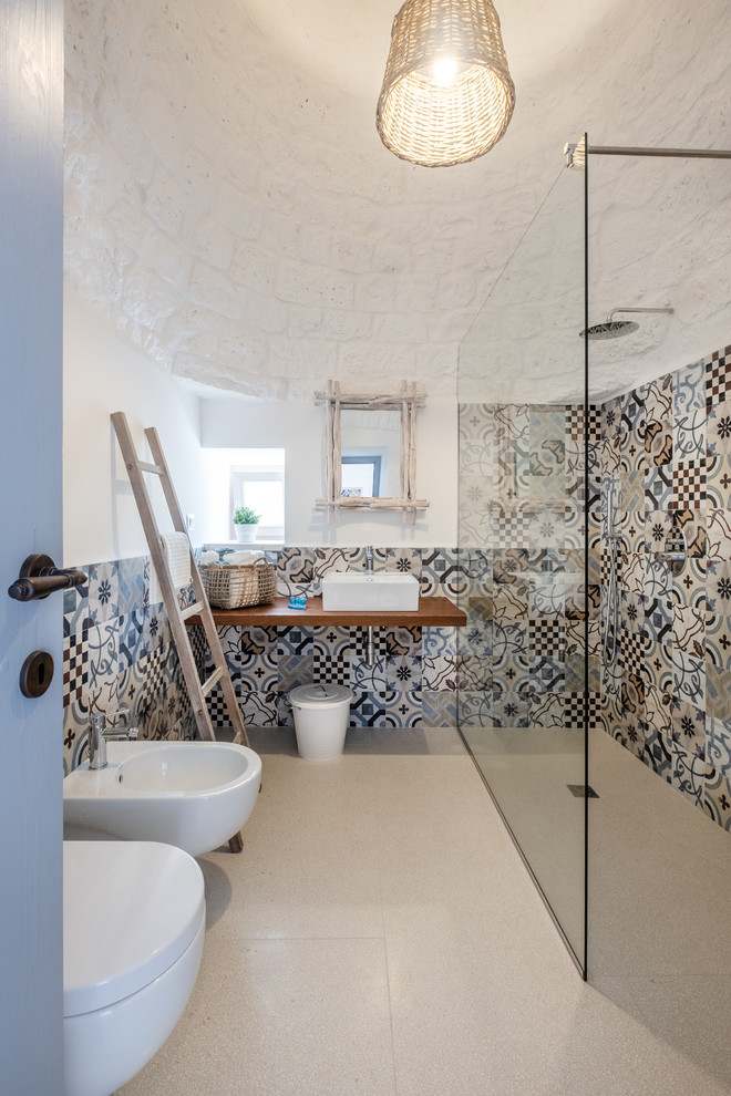 Inspiration for a mediterranean 3/4 bathroom in Bari with a corner shower, a bidet, multi-coloured tile, cement tile, white walls, a vessel sink, wood benchtops, beige floor, an open shower and brown benchtops.