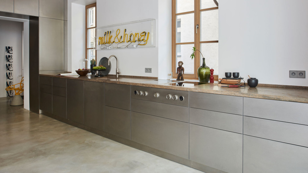 This is an example of a modern single-wall kitchen in Munich with flat-panel cabinets, stainless steel cabinets, granite benchtops, white splashback, black appliances, grey floor, beige benchtop and exposed beam.