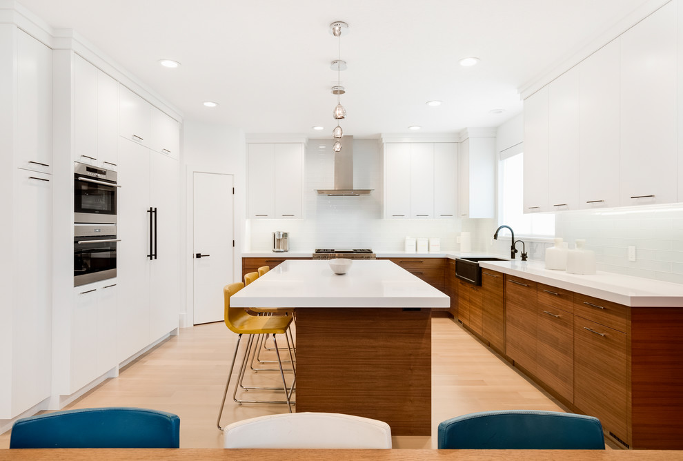 This is an example of a contemporary kitchen in Salt Lake City with flat-panel cabinets, medium wood cabinets, with island, a farmhouse sink, white splashback, stainless steel appliances, light hardwood floors and white benchtop.