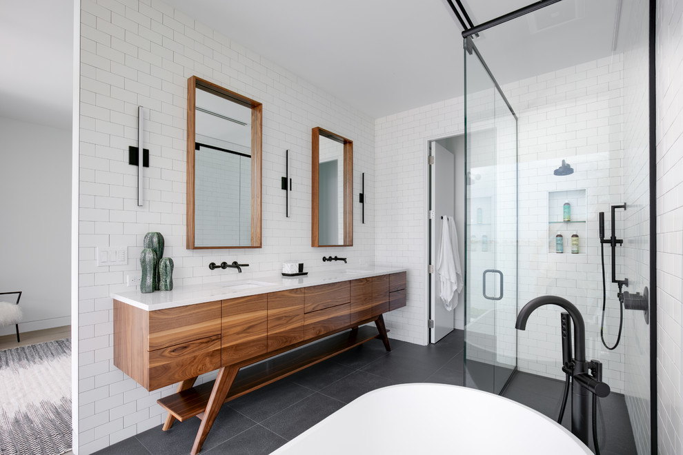 Design ideas for a mid-sized contemporary bathroom in Tampa with flat-panel cabinets, medium wood cabinets, a freestanding tub, white tile, subway tile, white walls, ceramic floors, an undermount sink, marble benchtops, black floor, a hinged shower door, white benchtops and a curbless shower.