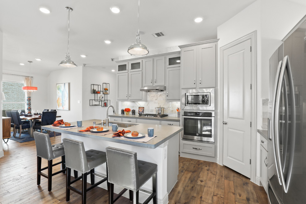 Mid-sized traditional l-shaped eat-in kitchen in Dallas with an undermount sink, shaker cabinets, grey cabinets, solid surface benchtops, white splashback, ceramic splashback, stainless steel appliances, medium hardwood floors, with island, beige floor and grey benchtop.