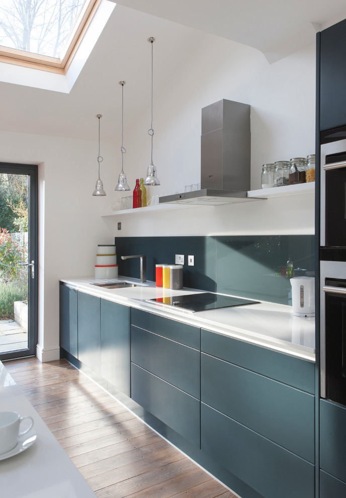 Design ideas for a medium sized contemporary single-wall kitchen/diner in London with an integrated sink, flat-panel cabinets, grey cabinets, composite countertops, grey splashback, glass sheet splashback, integrated appliances, an island, brown floors, white worktops and feature lighting.