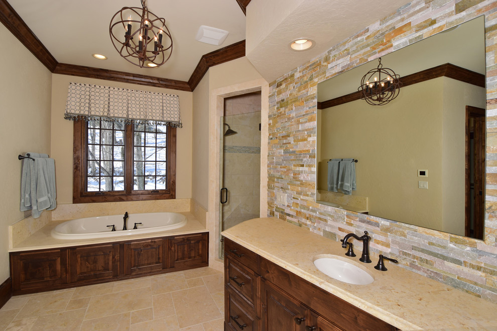 This is an example of an expansive country master bathroom in Charlotte with an undermount sink, raised-panel cabinets, dark wood cabinets, granite benchtops, a drop-in tub, a double shower, a two-piece toilet, beige tile, stone tile, beige walls and travertine floors.
