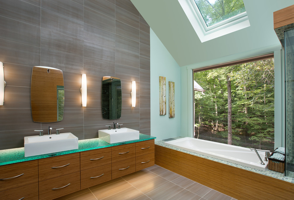 This is an example of a contemporary master bathroom in Columbus with a vessel sink, flat-panel cabinets, medium wood cabinets, glass benchtops, a drop-in tub and blue walls.