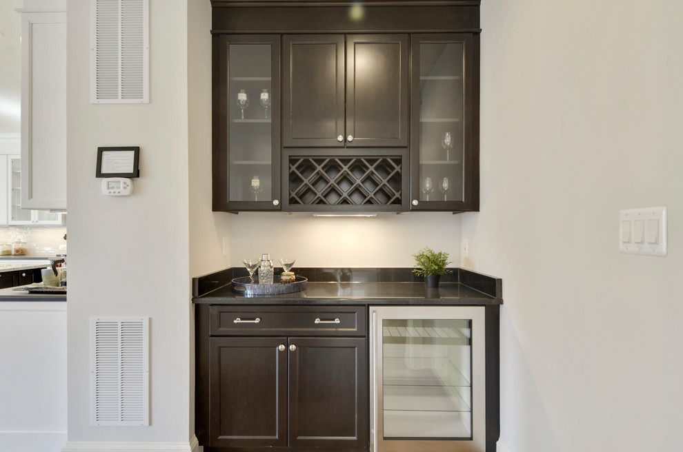 This is an example of a small transitional single-wall wet bar in DC Metro with recessed-panel cabinets, dark wood cabinets, granite benchtops, medium hardwood floors and grey benchtop.