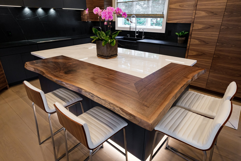 Large contemporary l-shaped kitchen/diner in New York with an integrated sink, flat-panel cabinets, medium wood cabinets, marble worktops, black splashback, stone slab splashback, integrated appliances, light hardwood flooring, an island and black worktops.