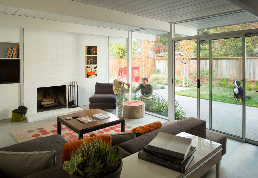 Design ideas for a mid-sized midcentury open concept living room in San Francisco with white walls, a standard fireplace, porcelain floors, a brick fireplace surround, a wall-mounted tv, grey floor and exposed beam.