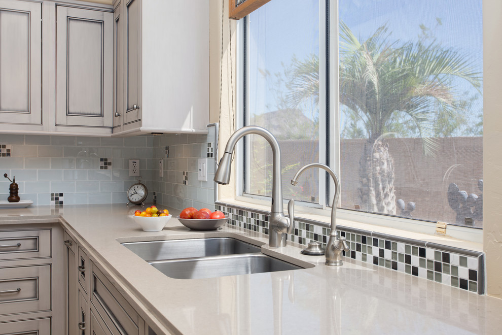 Example of a large transitional l-shaped ceramic tile open concept kitchen design in Phoenix with an undermount sink, beaded inset cabinets, gray cabinets, quartz countertops, white backsplash, glass tile backsplash, black appliances and an island