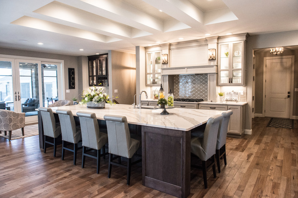 Example of a huge transitional l-shaped medium tone wood floor and brown floor open concept kitchen design with a single-bowl sink, glass-front cabinets, gray cabinets, quartz countertops, gray backsplash, ceramic backsplash, stainless steel appliances, an island and white countertops