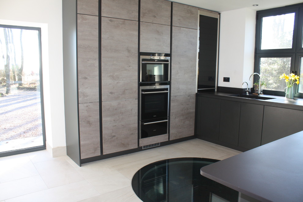 This is an example of a mid-sized modern u-shaped open plan kitchen in Other with a peninsula, an undermount sink, flat-panel cabinets, grey cabinets, solid surface benchtops, grey splashback, black appliances, ceramic floors, engineered quartz splashback, grey floor, grey benchtop and coffered.