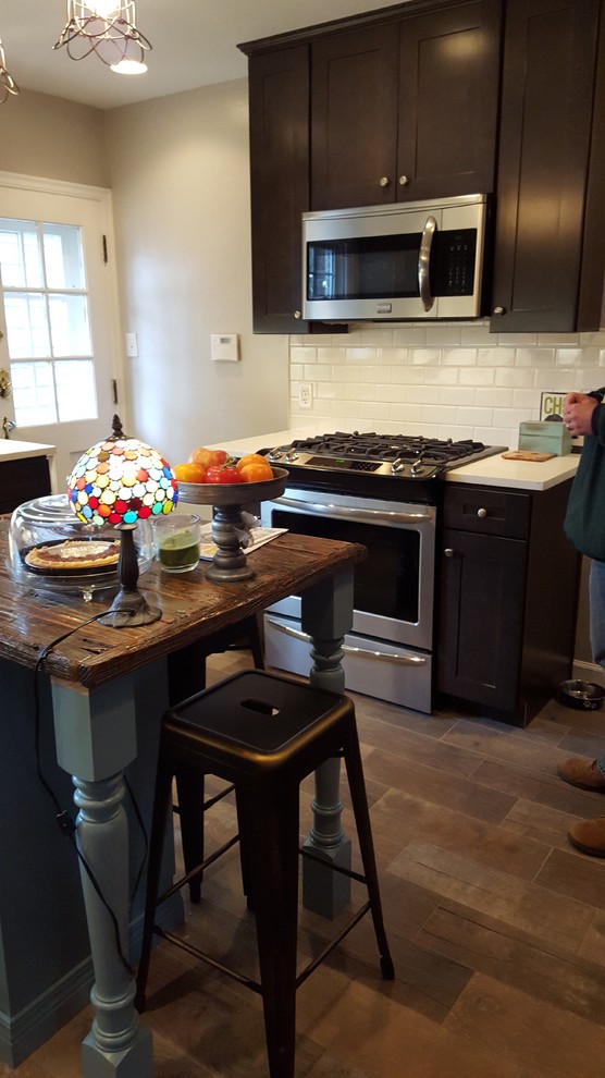 Inspiration for a mid-sized rustic u-shaped porcelain tile eat-in kitchen remodel in Indianapolis with a farmhouse sink, shaker cabinets, dark wood cabinets, wood countertops, white backsplash, ceramic backsplash, stainless steel appliances and an island