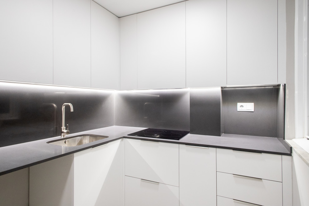 Idéer för ett avskilt, mellanstort modernt grå l-kök, med en enkel diskho, släta luckor, vita skåp, grått stänkskydd, svarta vitvaror, klinkergolv i keramik och grått golv