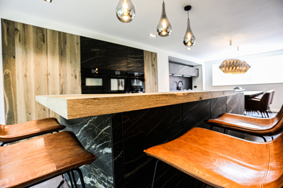 Photo of a large modern galley kitchen/diner in Other with flat-panel cabinets, medium wood cabinets, marble worktops, porcelain flooring, an island, black floors and black worktops.