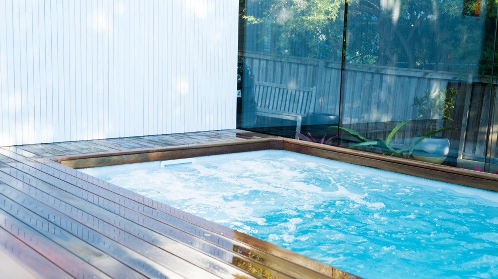 Modelo de piscina minimalista pequeña rectangular en patio trasero con paisajismo de piscina y entablado
