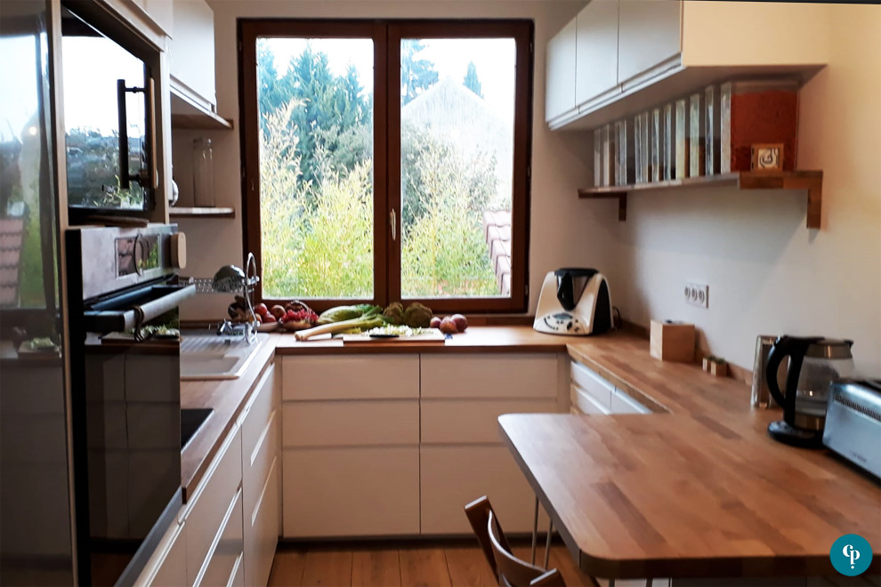 This is an example of a mid-sized scandinavian u-shaped separate kitchen in Paris with a double-bowl sink, beaded inset cabinets, white cabinets, wood benchtops, metallic splashback, mirror splashback, stainless steel appliances, light hardwood floors, no island, beige floor and brown benchtop.