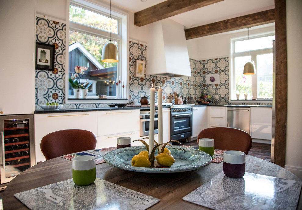This is an example of a mid-sized country u-shaped eat-in kitchen with an undermount sink, flat-panel cabinets, white cabinets, soapstone benchtops, multi-coloured splashback, cement tile splashback, stainless steel appliances, brick floors, no island and red floor.