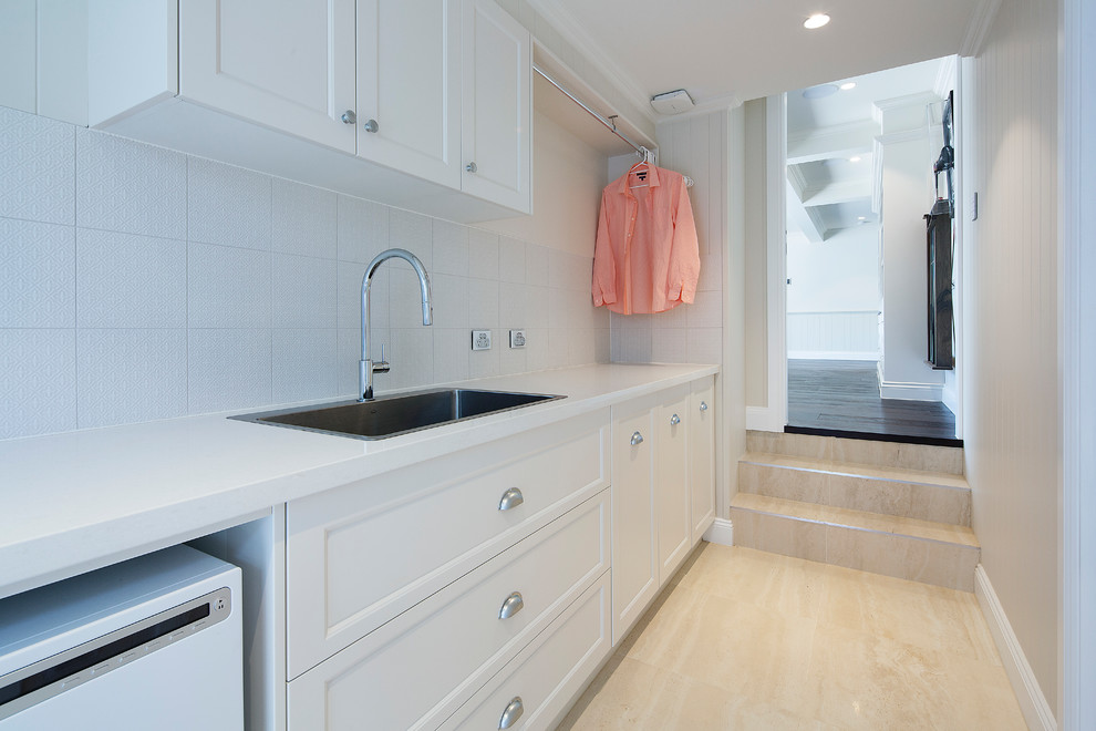 Design ideas for a mid-sized beach style galley dedicated laundry room in Brisbane with a drop-in sink, shaker cabinets, white cabinets, quartz benchtops, beige walls, porcelain floors, a side-by-side washer and dryer, beige floor and white benchtop.