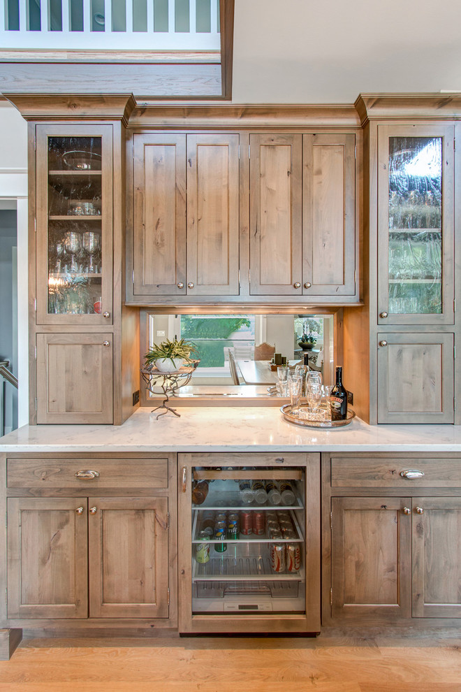 Mid-sized country single-wall home bar in Milwaukee with flat-panel cabinets, beige cabinets, quartz benchtops, mirror splashback and medium hardwood floors.