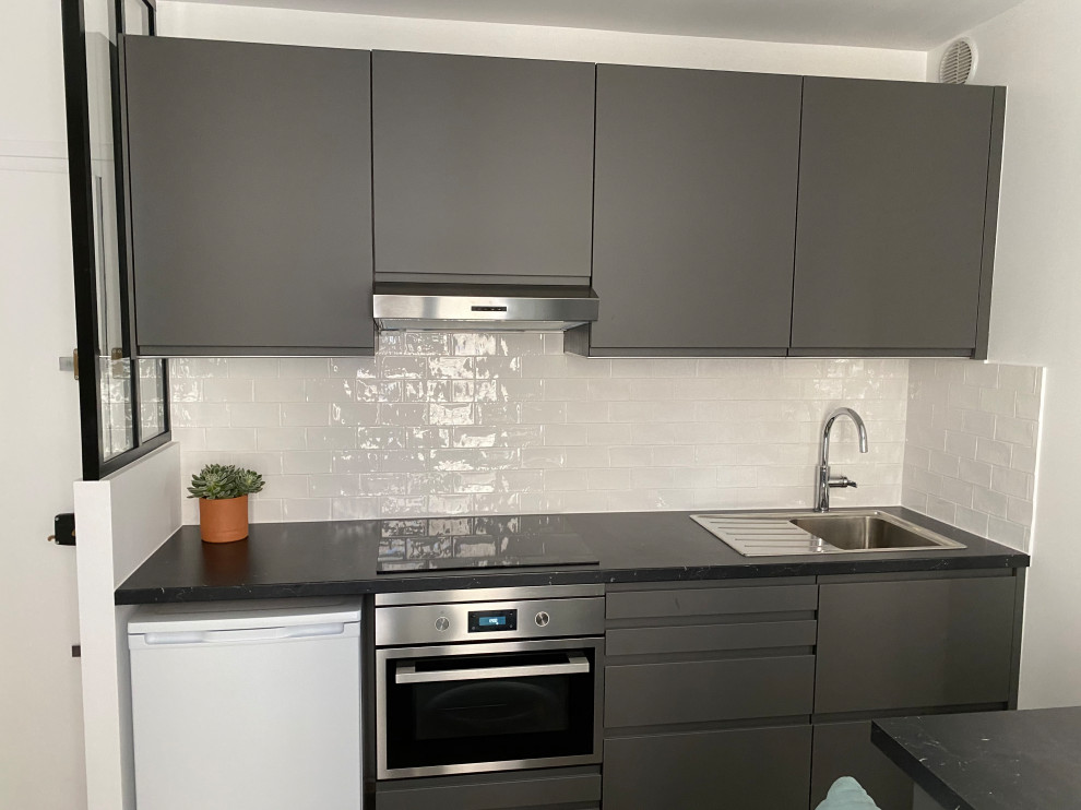 Photo of a small contemporary single-wall open plan kitchen in Paris with a single-bowl sink, beaded inset cabinets, grey cabinets, laminate benchtops, black splashback, porcelain splashback, ceramic floors, with island, beige floor and exposed beam.