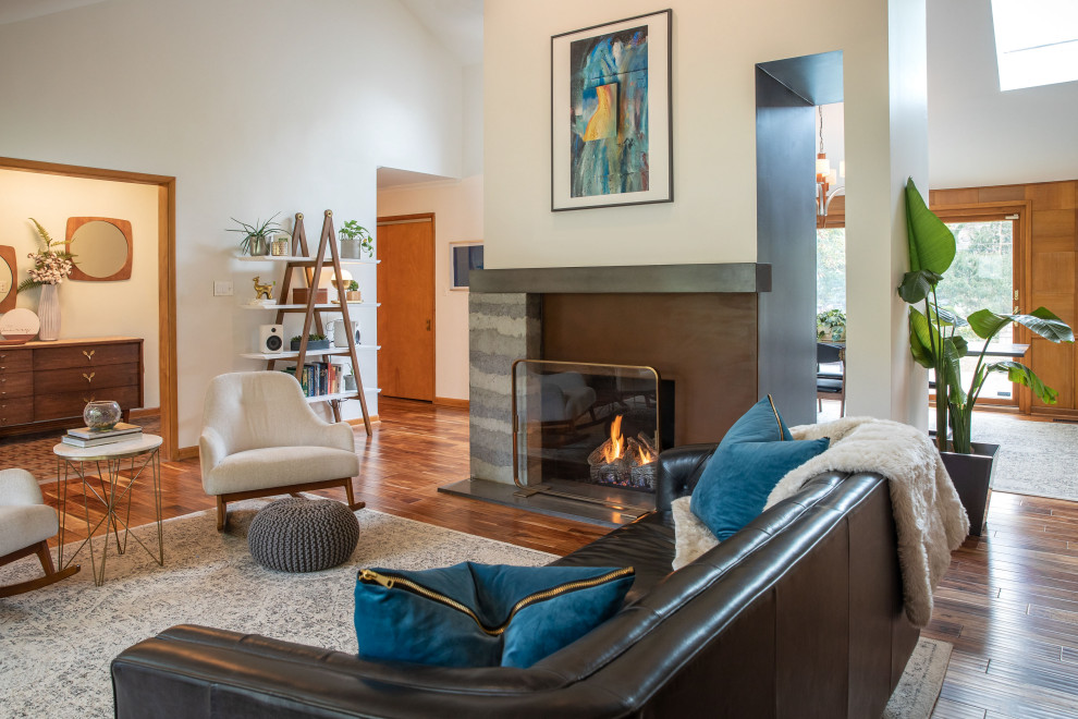 Photo of a mid-sized midcentury open concept living room in Indianapolis with beige walls, medium hardwood floors, a concrete fireplace surround, brown floor, a standard fireplace and vaulted.
