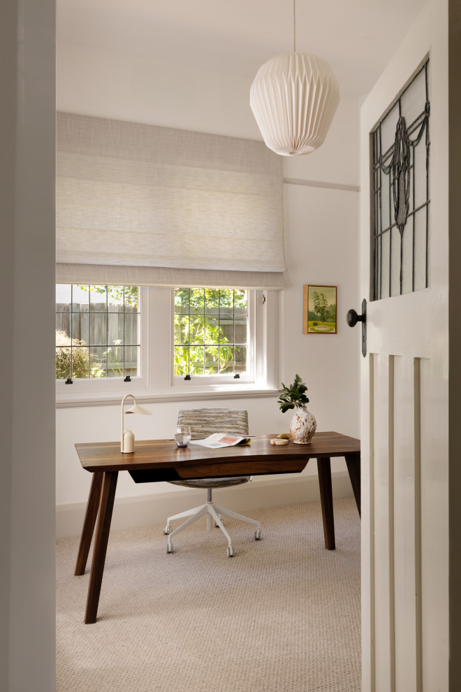 This is an example of a transitional home office in Melbourne with white walls, carpet, a freestanding desk and beige floor.