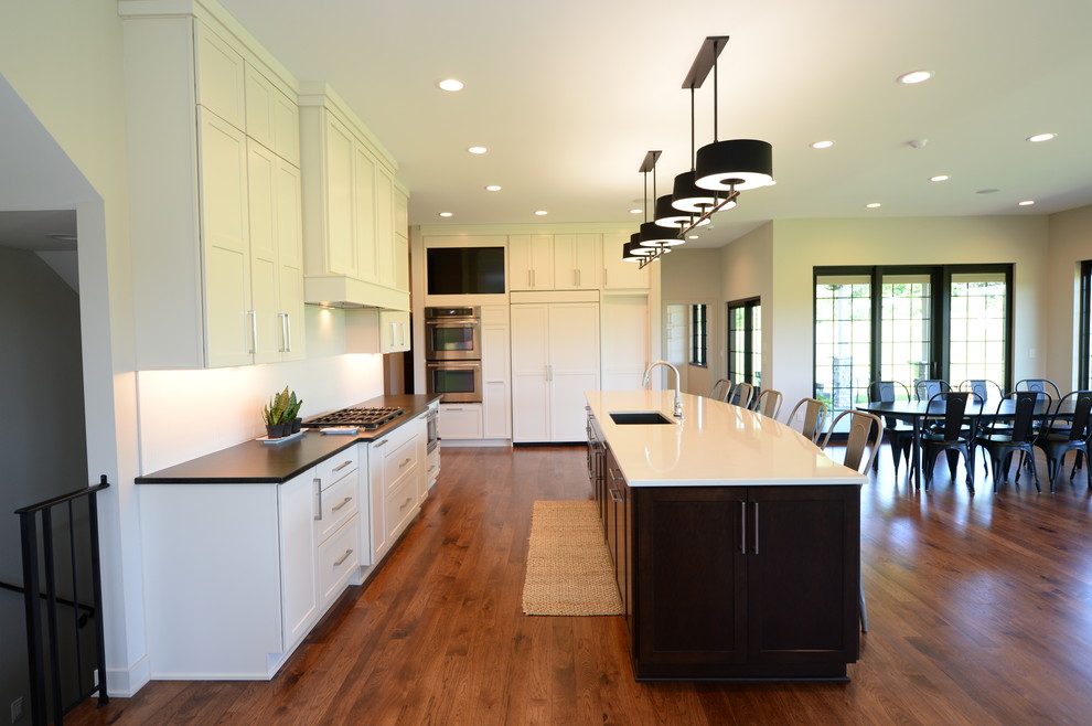 Inspiration for a large transitional single-wall medium tone wood floor open concept kitchen remodel with an undermount sink, recessed-panel cabinets, white cabinets, granite countertops, white backsplash, stainless steel appliances and an island