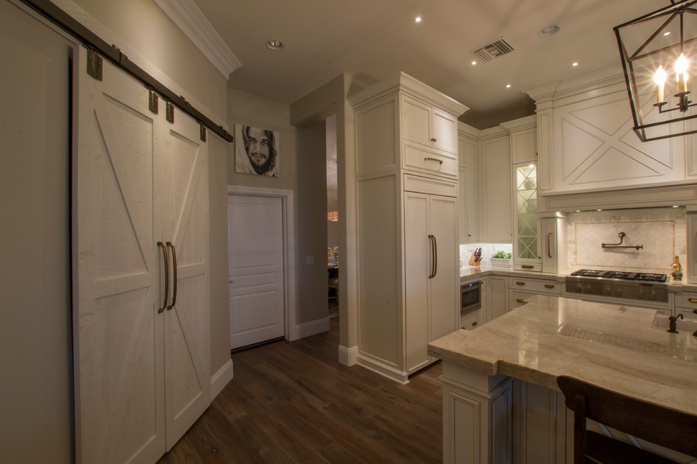 This is an example of a large country l-shaped open plan kitchen in Phoenix with a farmhouse sink, white cabinets, quartzite benchtops, stone tile splashback, stainless steel appliances, medium hardwood floors, with island, recessed-panel cabinets and white splashback.