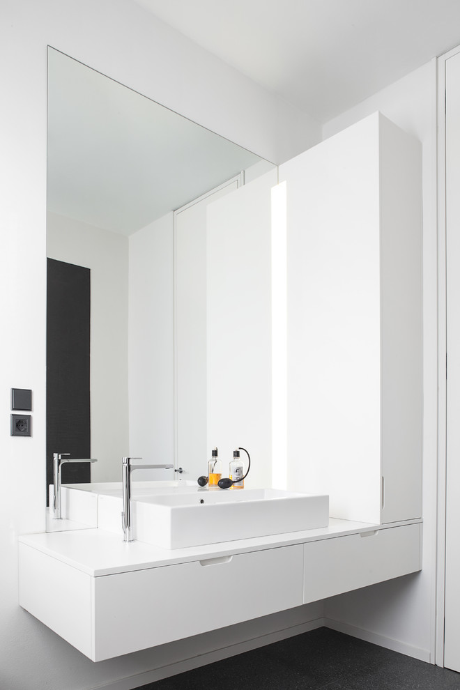 Photo of a large contemporary master bathroom in London with a vessel sink, flat-panel cabinets, white cabinets, a freestanding tub, a two-piece toilet, black tile and white walls.