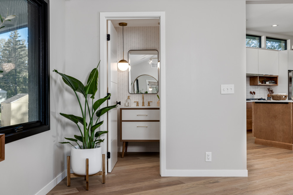 Photo of a small retro cloakroom in Minneapolis with flat-panel cabinets, medium wood cabinets, a wall mounted toilet, white walls, light hardwood flooring, a submerged sink, engineered stone worktops, beige floors, white worktops, a freestanding vanity unit and wallpapered walls.