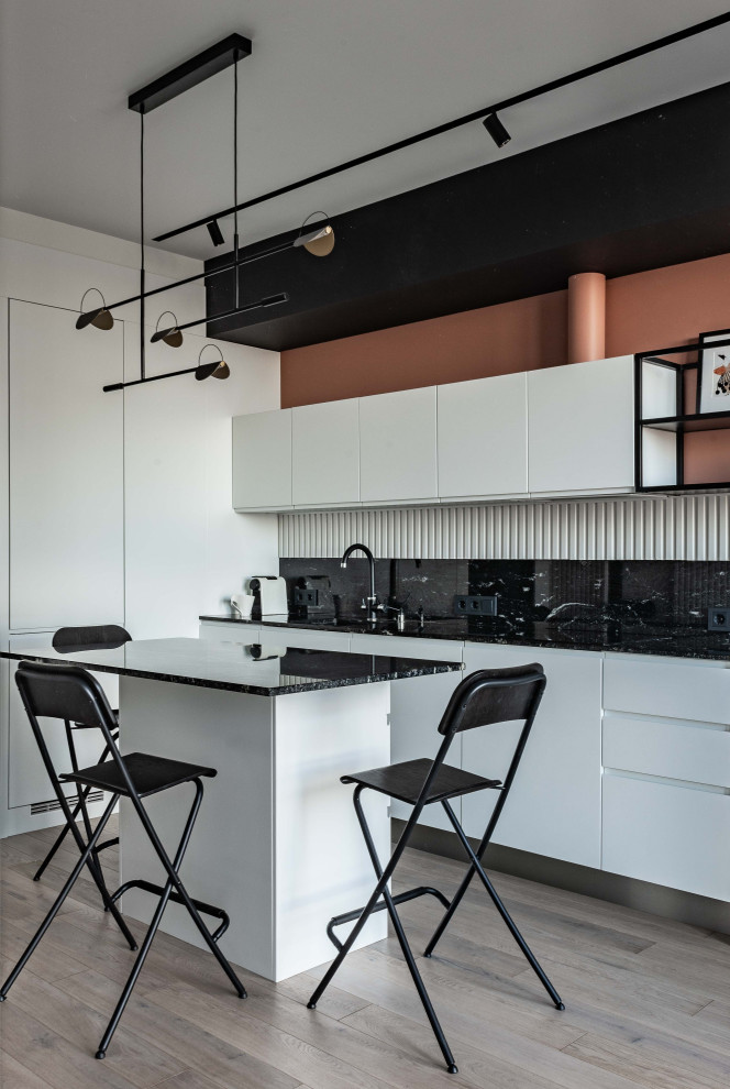 This is an example of a small contemporary single-wall eat-in kitchen in Moscow with flat-panel cabinets, white cabinets, light hardwood floors, with island, beige floor, black benchtop, an undermount sink, granite benchtops, black splashback, granite splashback and black appliances.