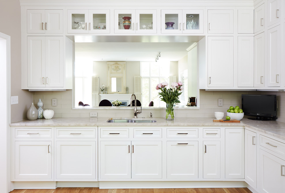 Photo of a mid-sized transitional l-shaped eat-in kitchen in DC Metro with white cabinets, beige splashback, subway tile splashback, stainless steel appliances and medium hardwood floors.