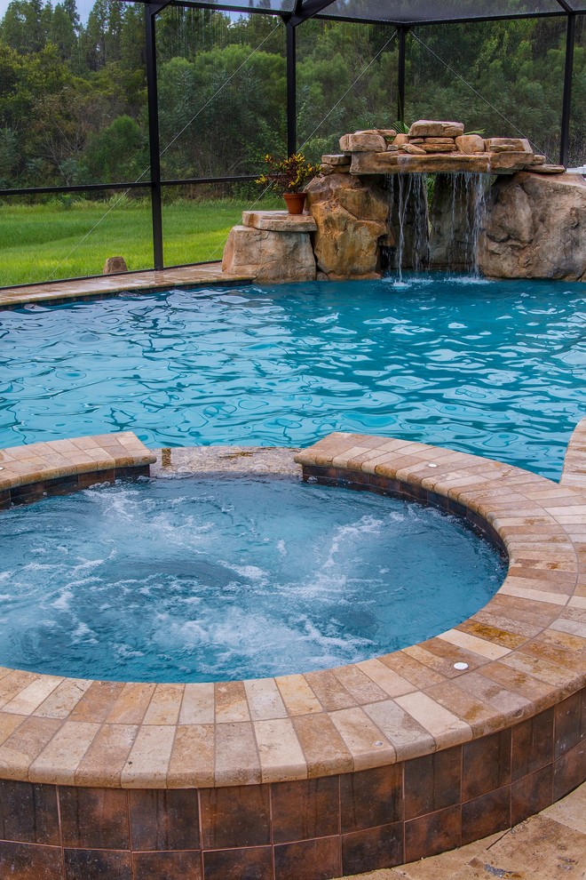 Photo of a large tropical backyard custom-shaped natural pool in Tampa with a water feature and natural stone pavers.