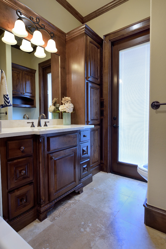 Large mediterranean master bathroom in Houston with raised-panel cabinets, dark wood cabinets, an alcove tub, a shower/bathtub combo, a one-piece toilet, beige tile, cement tile, beige walls, travertine floors, an undermount sink, marble benchtops, beige floor and a shower curtain.
