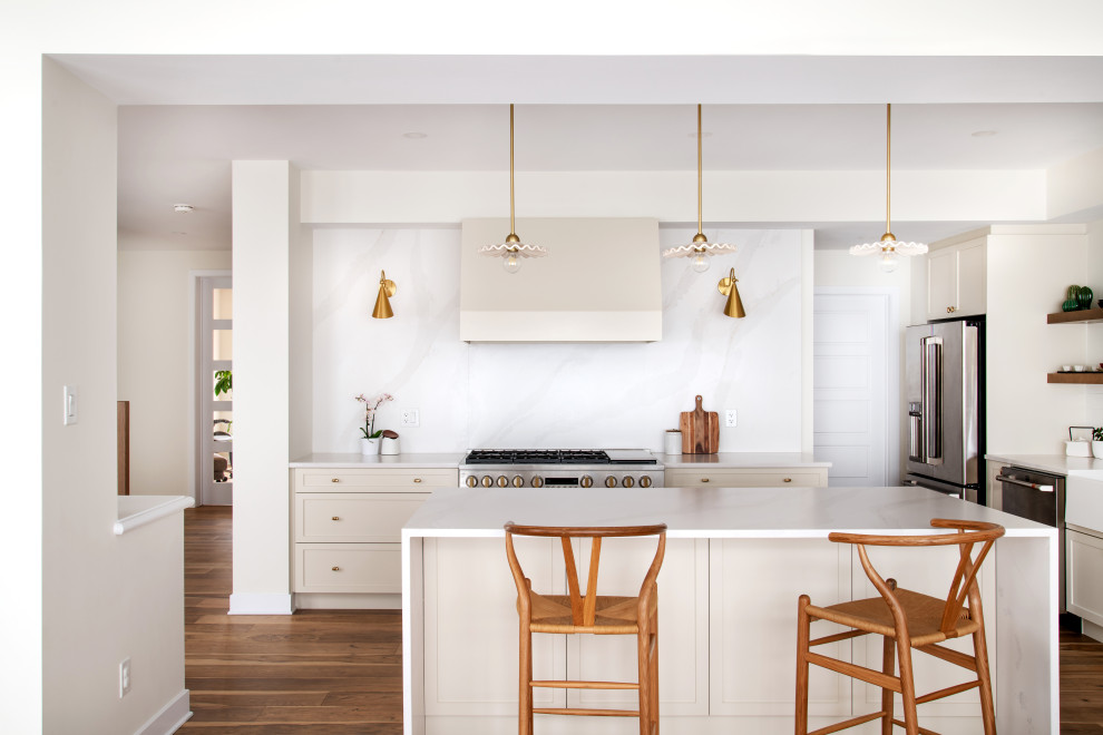 This is an example of a large scandinavian l-shaped kitchen/diner in Toronto with a belfast sink, shaker cabinets, white cabinets, engineered stone countertops, white splashback, engineered quartz splashback, stainless steel appliances, medium hardwood flooring, an island, brown floors and white worktops.