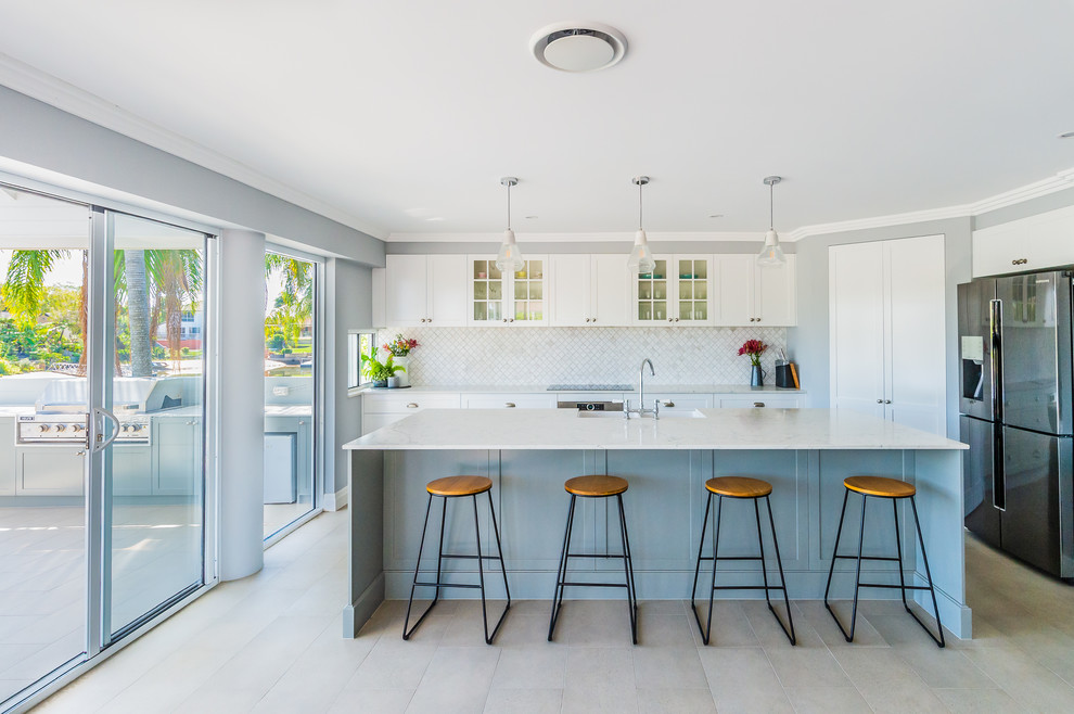 Beach style kitchen in Gold Coast - Tweed with glass-front cabinets, white cabinets, grey splashback, stainless steel appliances, with island, beige floor and grey benchtop.