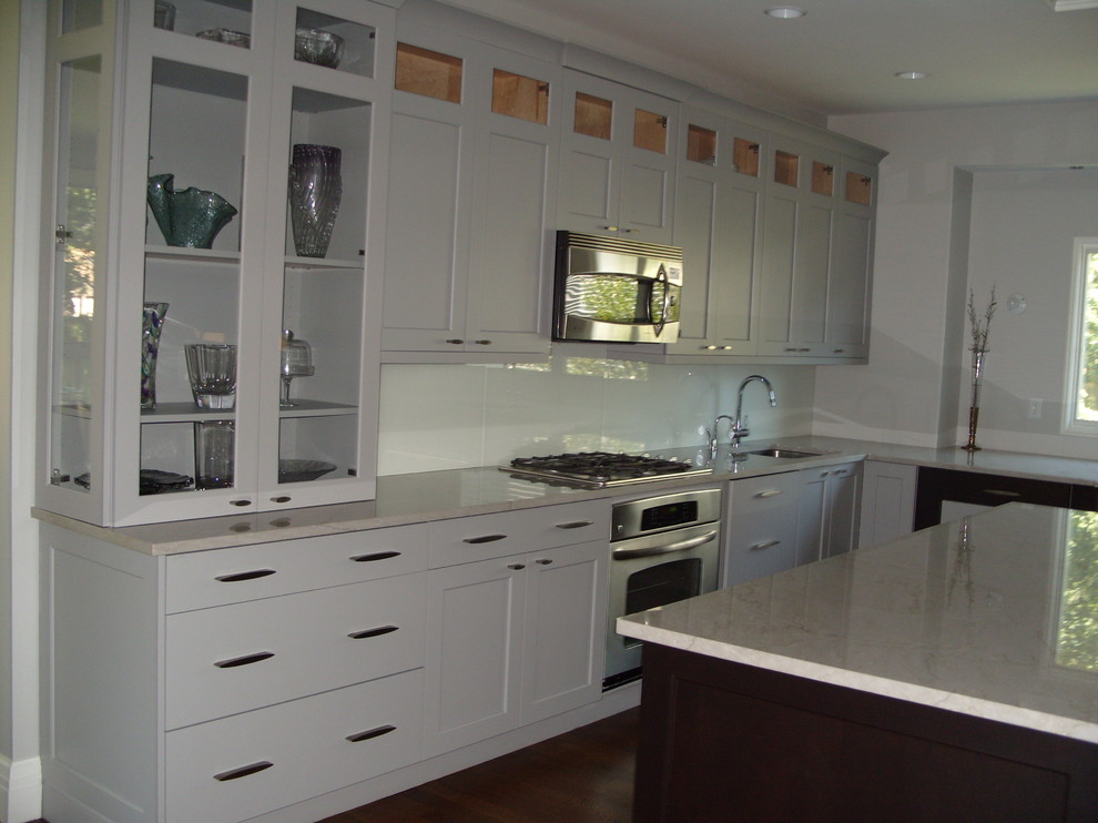 Large transitional medium tone wood floor kitchen photo in New York with shaker cabinets, white cabinets, white backsplash, glass tile backsplash, stainless steel appliances and an island