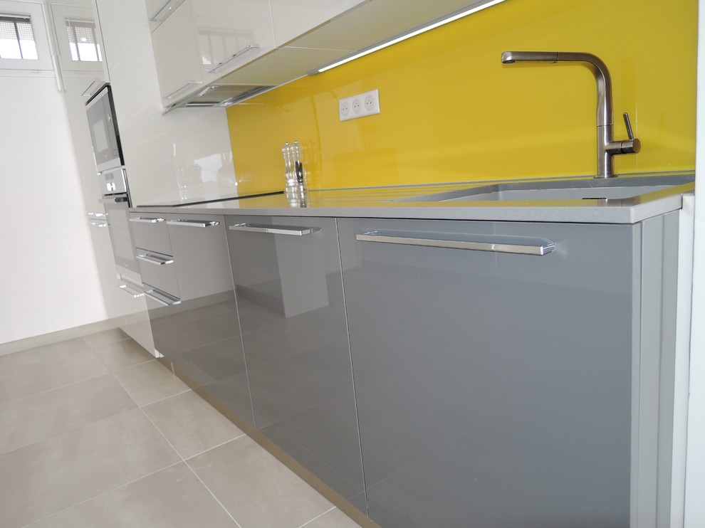 This is an example of a mid-sized modern single-wall open plan kitchen in Montpellier with an undermount sink, grey cabinets, quartzite benchtops, yellow splashback, glass sheet splashback, panelled appliances, ceramic floors and no island.