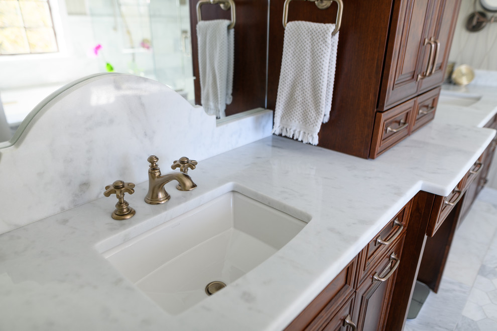 Mid-sized transitional master white tile and marble tile marble floor and white floor corner shower photo with raised-panel cabinets, dark wood cabinets, an undermount tub, gray walls, an undermount sink, quartzite countertops, a hinged shower door and white countertops