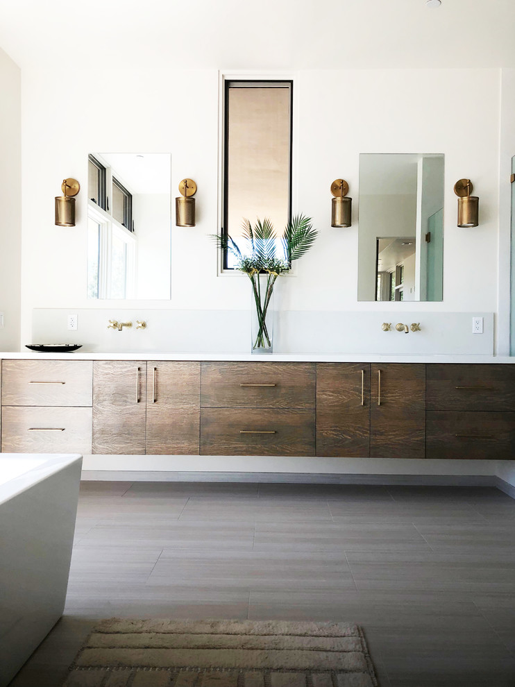 Photo of a large contemporary master bathroom in Santa Barbara with flat-panel cabinets, medium wood cabinets, a freestanding tub, a curbless shower, a one-piece toilet, white walls, porcelain floors, an undermount sink, engineered quartz benchtops, white floor, a hinged shower door and white benchtops.