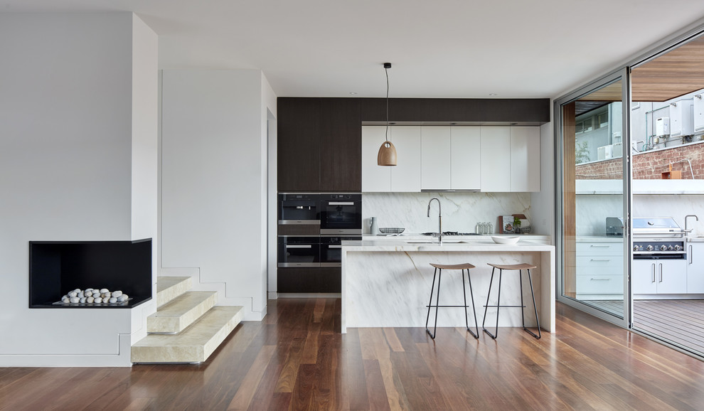 Photo of a mid-sized contemporary galley kitchen in Melbourne with an undermount sink, marble benchtops, white splashback, marble splashback, black appliances, medium hardwood floors, brown floor, white benchtop, flat-panel cabinets, dark wood cabinets and with island.