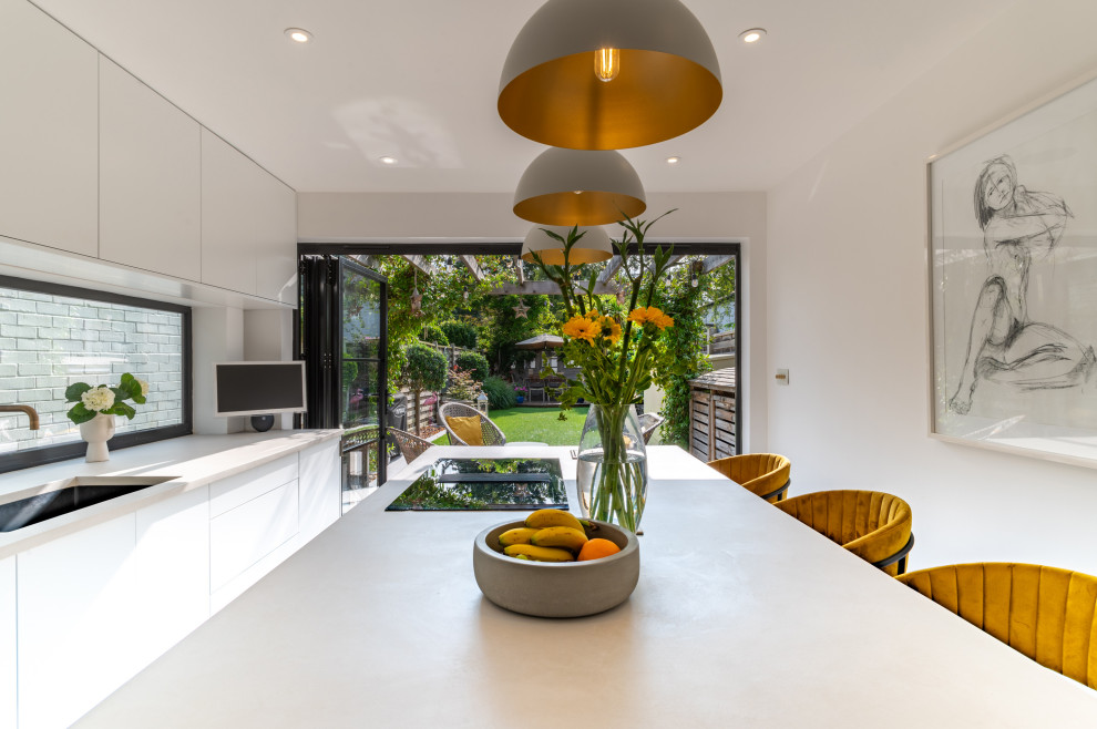 This is an example of a large contemporary single-wall open plan kitchen in London with flat-panel cabinets, white cabinets, black appliances, porcelain floors, multiple islands, grey floor and white benchtop.