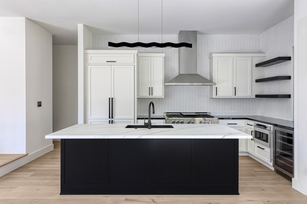This is an example of a medium sized modern l-shaped open plan kitchen in Austin with a submerged sink, shaker cabinets, black cabinets, engineered stone countertops, white splashback, stone tiled splashback, stainless steel appliances, light hardwood flooring, an island, beige floors, black worktops and a vaulted ceiling.