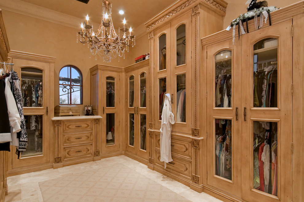 This is an example of an expansive mediterranean women's dressing room in Phoenix with raised-panel cabinets, light wood cabinets and travertine floors.