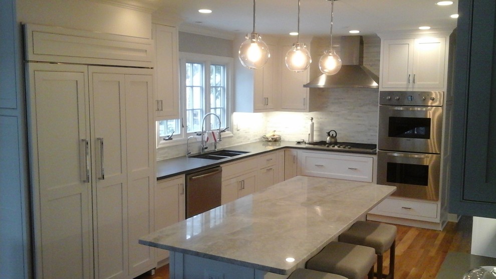 Inspiration for a mid-sized transitional l-shaped light wood floor eat-in kitchen remodel in Newark with a double-bowl sink, shaker cabinets, white cabinets, solid surface countertops, multicolored backsplash, stone tile backsplash, stainless steel appliances and an island
